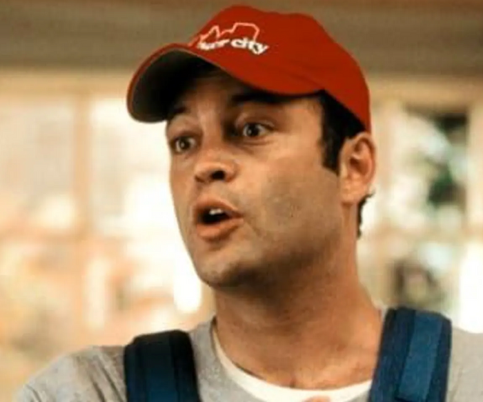 A man, the character Beanie from the 2003 comedy movie 'Old School' played by Vince Vaughn, wearing a red trucker hat that says 'Speaker City' underneath the outline of a city skyline.