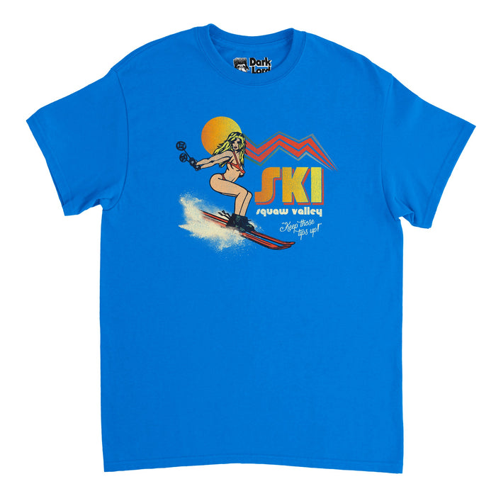 A vintage, bright blue t-shirt that says "Ski" in hombre yellow/orange bold letters above "Squaw Valley" and the catch phrase "Keep those tips up!" Includes the image of a girl skiing down a snowy hill in red skis and a red bikini, her skiing poles flying out behind her, drawn as if from a comic book, a orange/yellow sun behind her head with red, pointed lines emanating, resembling a mountain range. References Squaw Valley Ski Resort, now known as Palisades Tahoe ski resort in CA's Sierra Nevada