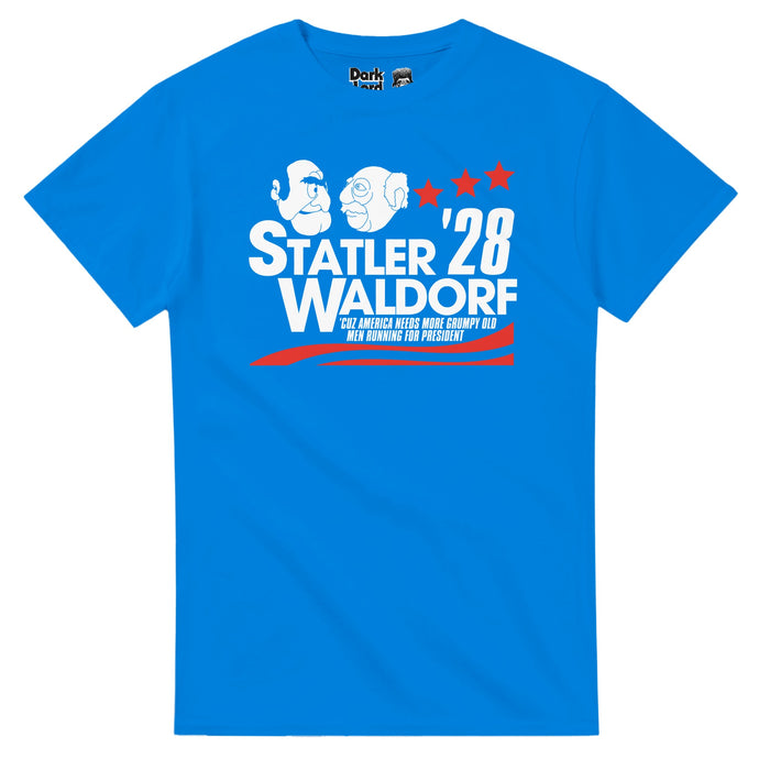 A retro, bright blue 70s style short sleeved t-shirt that says "Statler Waldorf '28, 'Cuz America Needs More Grumpy Old Men Running For President" with an image of the two iconic muppets, always bickering, staring at each other, and with red colored campaigning graphics like stars & stripes on the shirt. References the iconic series "The Muppet Show" and the always negative Statler and Waldorf who ran for president, performed by multiple acotrs including Richard Hunt, Jerry Nelson, Jim Henson, &