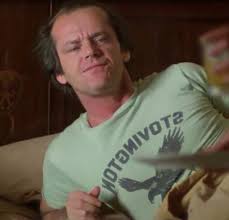 A man, Jack Torrance (played by actor Jack Nicholson) laying down on a couch in a light green "Stovington Eagles" t-shirt with the image of an eagle, referencing the prep school from Vermont, from the classic horror film "The Shining", based on the novel by Stephen King.