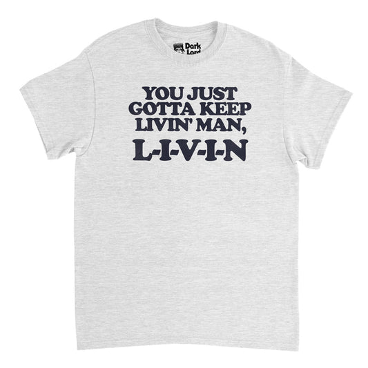 A retro, heather gray 70s style t-shirt that says "You Just Gotta Keep Livin' Man, L-I-V-I-N", referencing the iconic line from the 1990's coming of age comedy film Dazed and Confused, written and directed by Richard Linklater. The phrase was spoken by a young Matthew McConaughey playing David Wooderson, and the film also stared Jason London, Ben Affleck, and Parkey Posey.