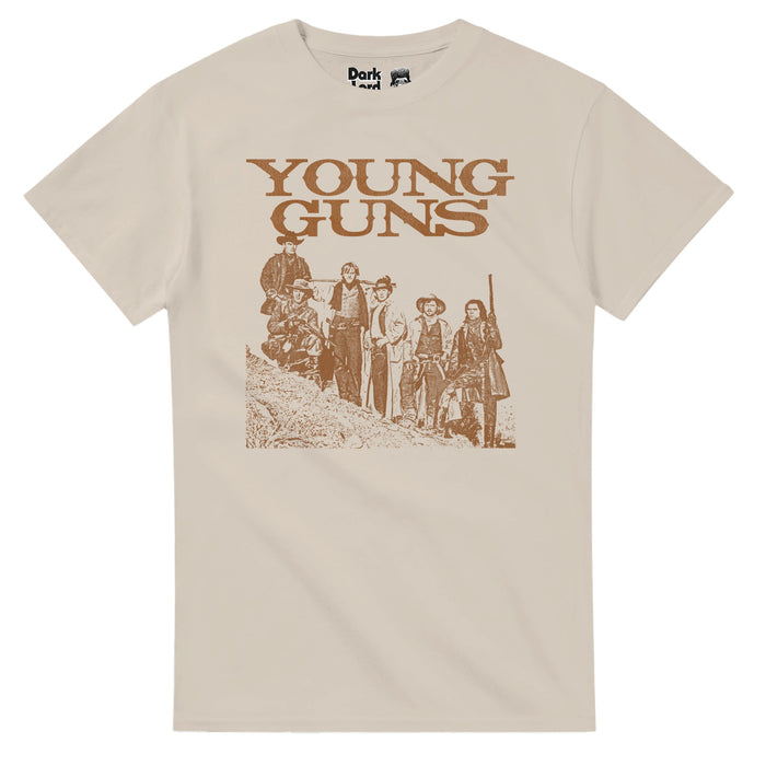 A sand colored, light brown Young Guns retro 80s style t-shirt with an image of six guys posed on the side of a New Mexico desert hill with cowboy hats and boots, some wielding guns. In reference to the iconic retelling of Billy the Kid and the Regulators from the Lincoln County War in the 1988 western film "Young Guns" starring iconic actors Emilio Estevez, Kiefer Sutherland, Lou Diamond Phillips, Charlie Sheen, Dermot Mulroney, and Casey Siemaszko.